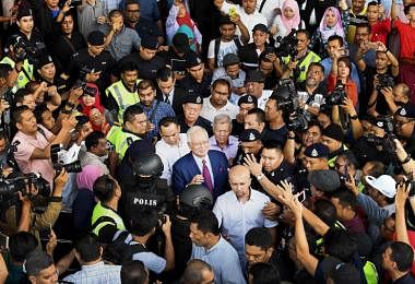 马来西亚前首相纳吉（中间戴眼镜）今天下午交保之后离开高庭时，被支持者和记者们里三层、外三层包围。