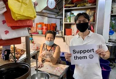 义顺集选区议员黄国光2020年6月拿着一张写着“支持他们”（Support Them）和画有笑脸的纸张，到小贩中心呼吁公众支持小贩